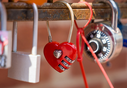 A red padlock with an engraved heart on a fence.