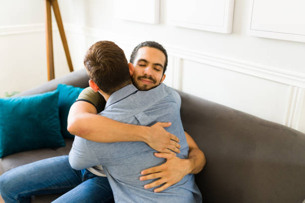 istock Romantic gay couple seen from behind hugging on the sofa 1418330365