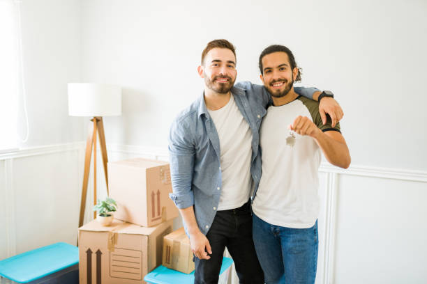 Cheerful gay couple buying a house together Portrait of a happy gay man and his boyfriend showing their new keys after buying a new house and moving in together key package stock pictures, royalty-free photos & images