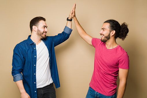 Cheerful gay couple making a high five smiling and celebrating doing a good work in their relationship