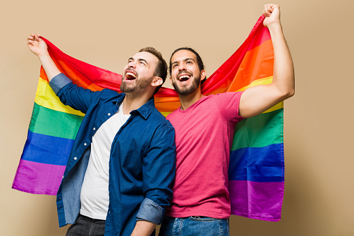 Very excited gay couple shouting and supporting the LGBT community while waving a rainbow flag