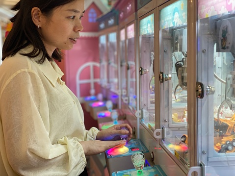 An Asian woman is playing with a doll machine