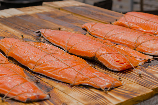 Hot smoked red salmon fish in row on wooden board at summer outdoor food festival, market: close up. Preparation, cookery, gastronomy and street food concept