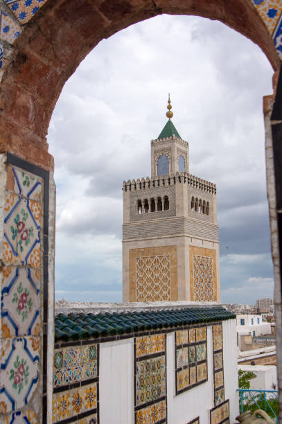 The Minaret of the Al-Zaytuna Mosque in Tunis, Tunisia with pigeons flying in the foreground.