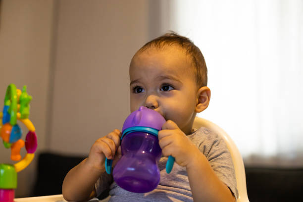 높은 아기 의자에 앉아 아기 병에서 물을 마시는 달콤한 아기 소년. 집에서 아기 - baby cup 뉴스 사진 이미지