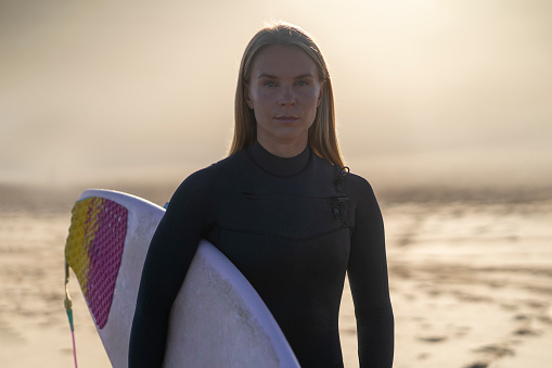 Surfer girl at the beach with her surfboard at sunrise. Female surfer woman