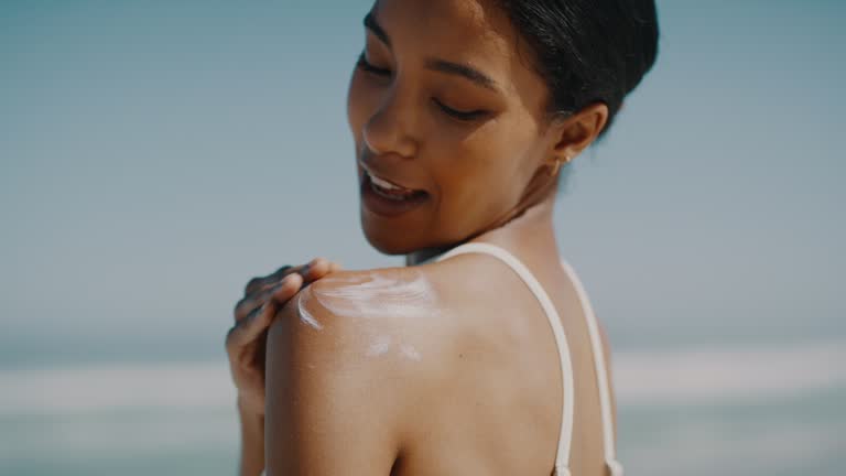 Skincare, fun and safety by woman apply sunscreen while on beach vacation, smiling and looking happy. Young female protect her skin from the summer sun while having fun relaxing on the seaside