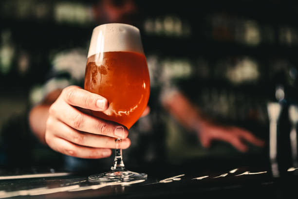 La main du barman tient un verre de bière plein dans un bar - Photo