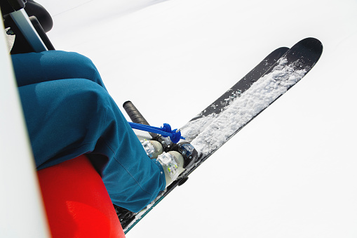 Legs of a skier with skis on the background of snow-covered fields. View from the cabin of the open lift. The concept of winter recreation and winter sports tourism.