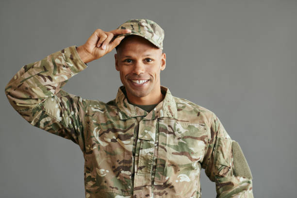 Young happy black soldier against gray background looking at camera.
