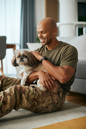 Happy African American military man enjoying with his dog at home.