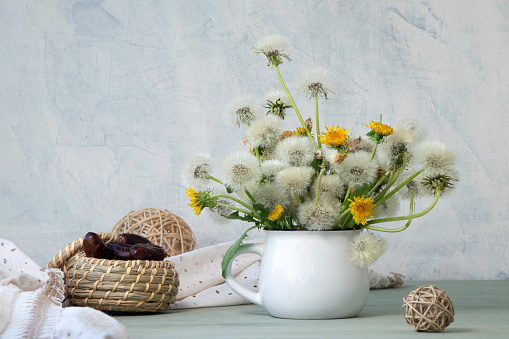 picturesque composition of dandelions in a mug on a white textured background. soft focus