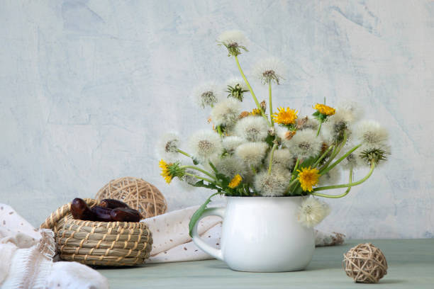 picturesque composition of dandelions in a mug on a white textured background. stock photo
