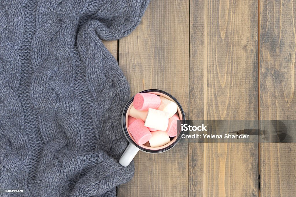 flat lay with mug full of marshmallows on wooden table with knitted warm gray plaid. autumn or winter concept. copy space. flat lay with mug full of marshmallows on wooden table with knitted warm gray plaid. autumn or winter concept. copy space. soft focus Affectionate Stock Photo