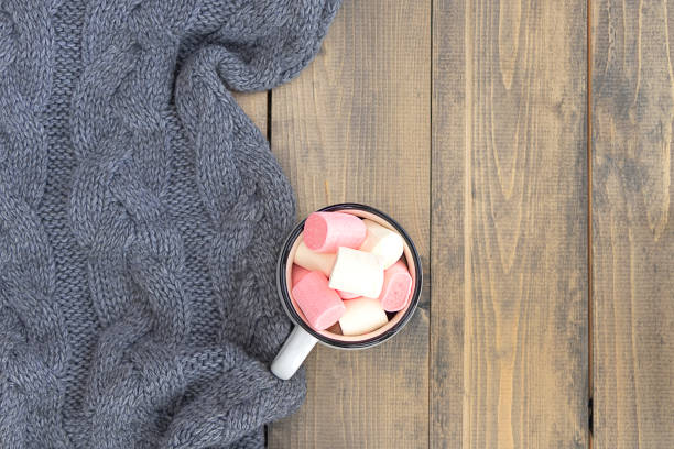 flat lay with mug full of marshmallows on wooden table with knitted warm gray plaid. autumn or winter concept. copy space. stock photo