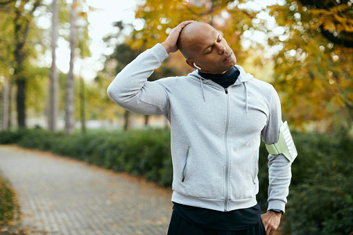 Young African American athlete warming up while exercising inthe park during autumn day. Copy space.