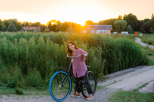 Young Caucasian woman riding bicycle on the bridge over the canal at sunset