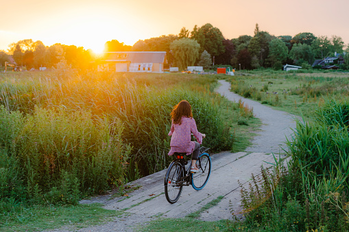 Young Caucasian woman riding bicycle on the bridge over the canal at sunset