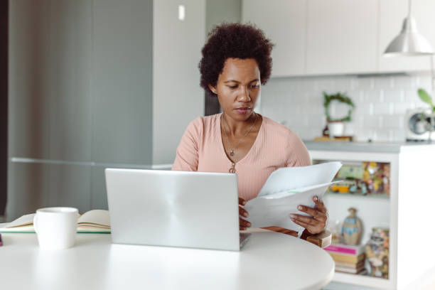 istock African-American holding papers and using laptop 1418406725