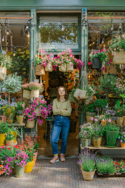 woman standing at the entrance of the flower shop - garden center flower women plant imagens e fotografias de stock