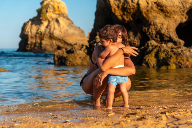 мать обнимает своего сына на пляже в прайя-дус-аррифес, пляж алгарве, албуфейра. португалия - алгарве стоковые фото и изображения