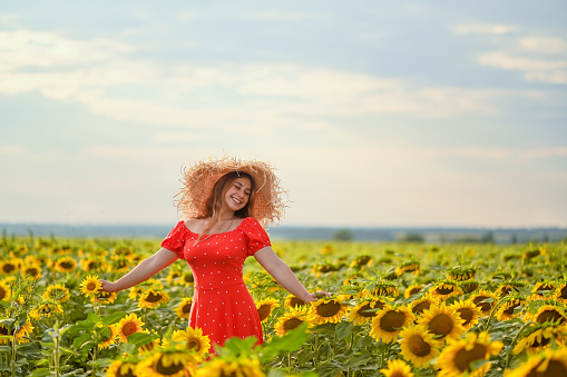 a sunflower field and a laughing girl in a red polka dot dress and a straw hat..