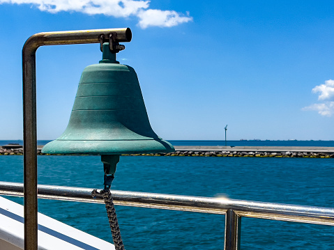 Close Up on a bronze bell hanging outside at the railing of a ferry boat. Beautiful blue sky with fluffy white clouds and sea background, copy space.