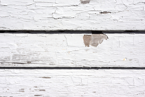 Worn wall of an old house with chipped and peeling paint showing bare wood underneath in the morning light.
