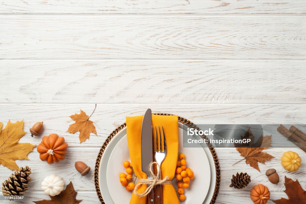 Thanksgiving day concept. Top view photo of plate cutlery fork knife napkin rowan maple leaves pine cones acorns pumpkins and cinnamon sticks on isolated white wooden table background with copyspace Thanksgiving - Holiday Stock Photo