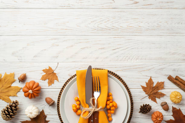 thanksgiving day concept. top view photo of plate cutlery fork knife napkin rowan maple leaves pine cones acorns pumpkins and cinnamon sticks on isolated white wooden table background with copyspace - plate food color image photography imagens e fotografias de stock