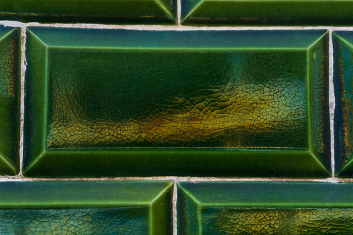 Background of old green tiles with cracks and iridescent tints close up