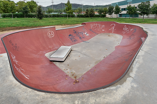 Viladecans, Catalunya, Spain - August 25, 2022: Concrete skate park skate park empty, with trees some graffiti and cloudy sky stock image.