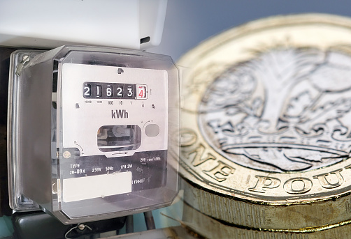 Electric power meter with pound coins overlaid - expensive fuel bills concept with multi-layered effect.