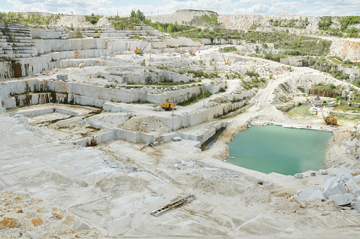 Above view of part of vast territory of modern quarry belonging to industrial production factory with small pond and machinery