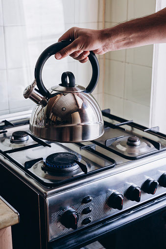Man's hand puts the kettle on the gas burner.