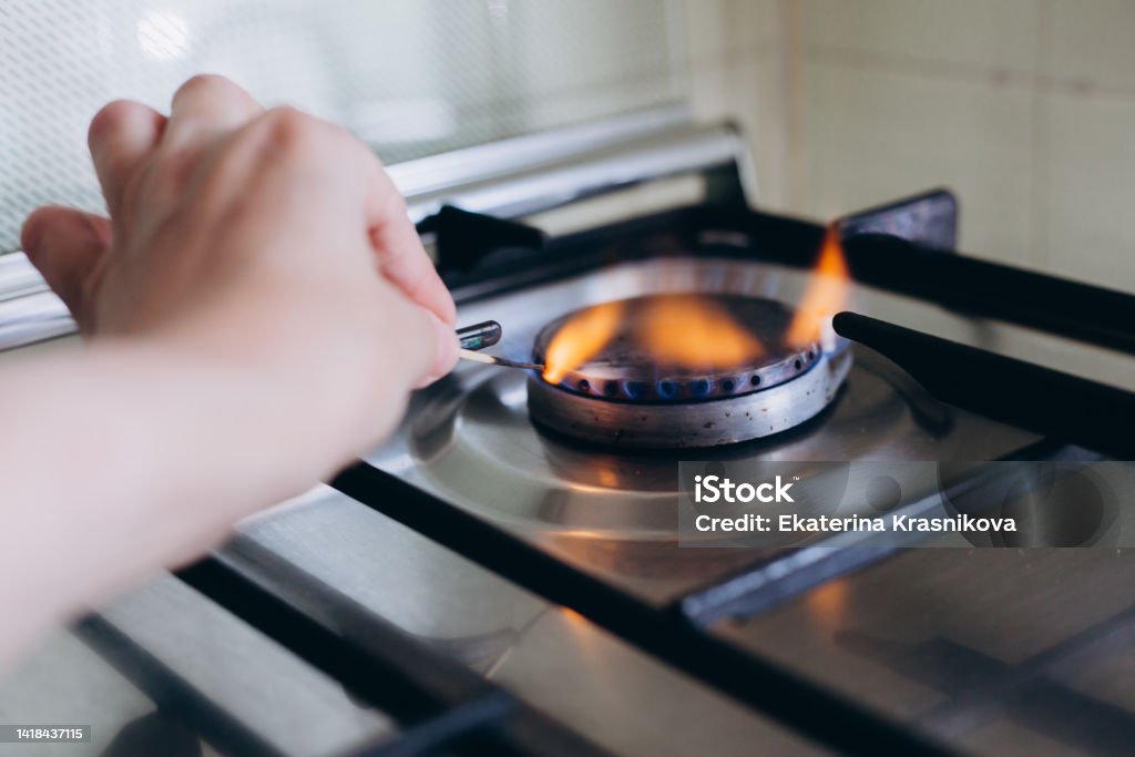 A woman's hand with matchstick lights gas stove in her apartment A woman's hand with matchstick lights gas stove in her apartment. Fuel Prices Stock Photo