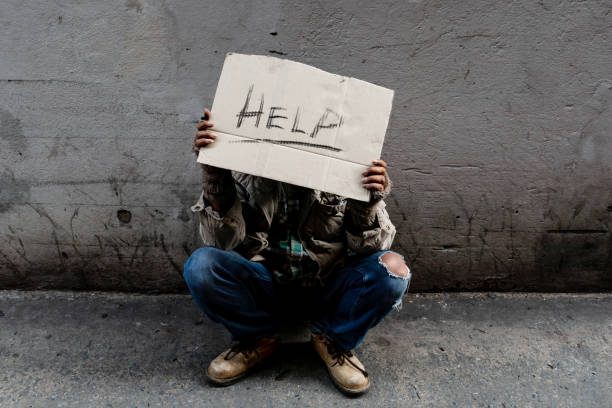 un hombre asiático sin hogar y de pelo largo se sienta irremediablemente apoyado contra una pared, ya que no hay nadie que lo ayude con el trabajo y la comida en la mano sosteniendo un letrero de ayuda. las personas sin hogar duermen en las calles - vagabundo fotografías e imágenes de stock