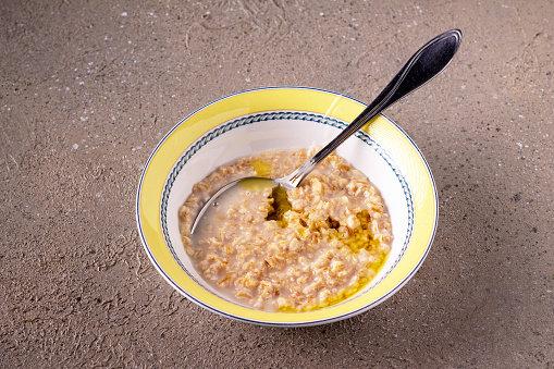 oatmeal porridge with olive oil in a round ceramic plate on a beige table