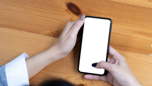 istock hand woman using a telephone, empty screen smart phone and computer on wooden table top view. 1418452946