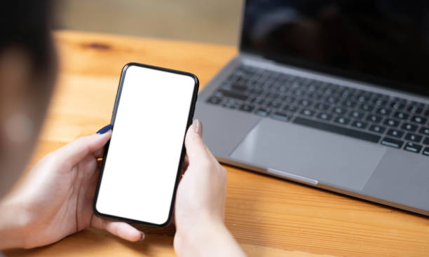 istock hand woman using a telephone, empty screen smart phone and computer on wooden table top view. 1418453051
