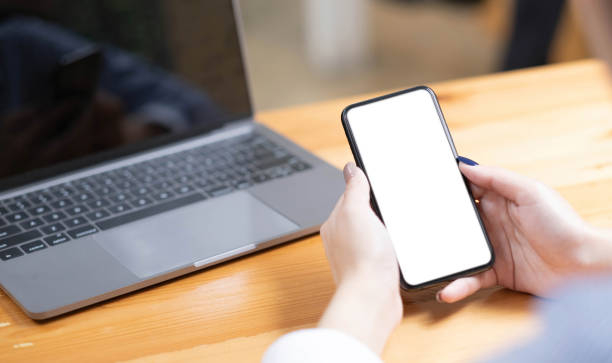 istock hand woman using a telephone, empty screen smart phone and computer on wooden table top view. 1418453125