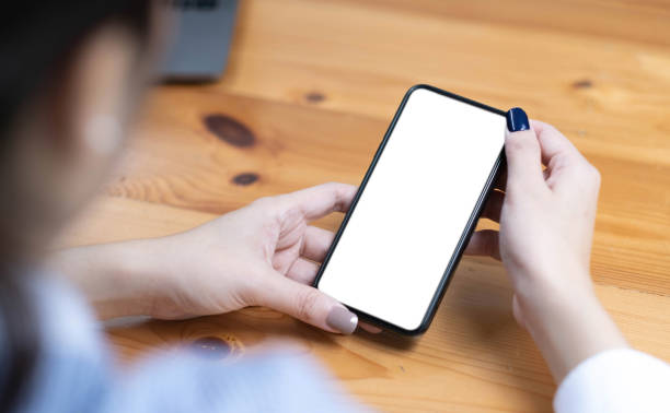 istock hand woman using a telephone, empty screen smart phone and computer on wooden table top view. 1418453213