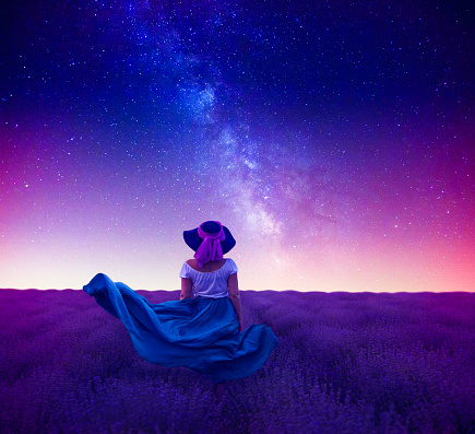 Composite image of a woman standing in a lavender field at night looking at the Milky Way.