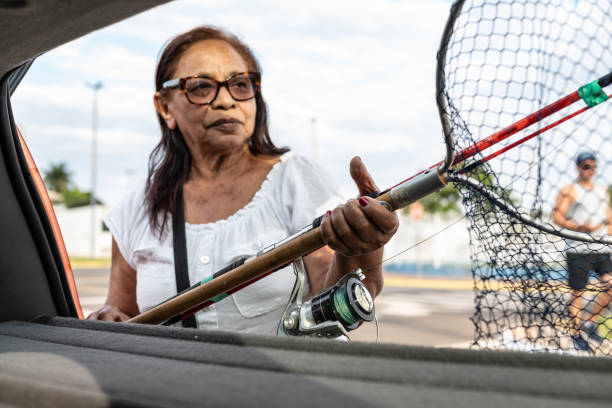 Portrait of a senior lady living an actively, going to a park to go fishing. She is leaving her car and taking her fishing equipments in the car trunk to go fishing.