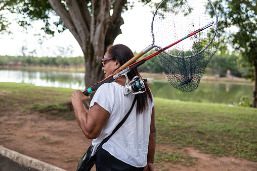 Portrait of a senior lady carrying a fishing rod and other fishing equipments, going to a lake to fish.