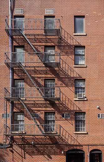 Brownstone wall with windows and fire escape staircases on a sunny day with graphic shadows