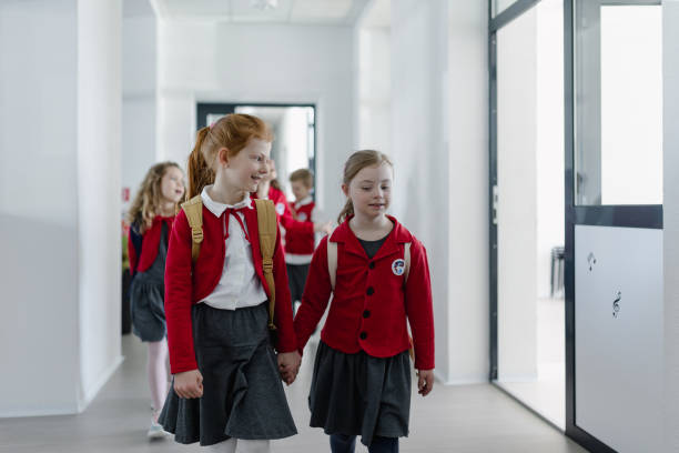 istock Happy schoolgrirl with Down syndrome in uniform walking in school corridor with her classmate, holding each other hands. 1418466029