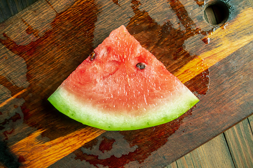 Sweet watermelon with pits on a wooden table. A triangular slice of watermelon on a wooden table. beautiful slice of watermelon.