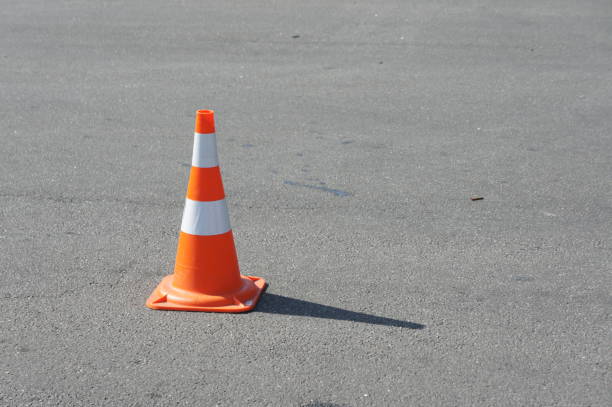 istock traffic cone, with white and orange stripes on gray asphalt, copy space. Bright weather 1418474345