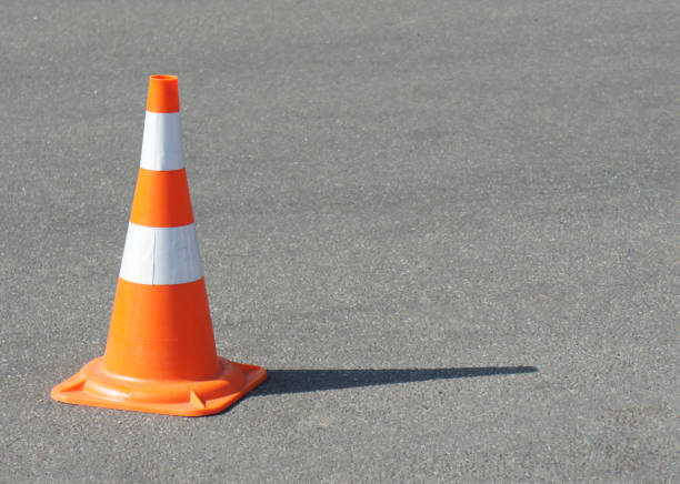 istock traffic cone, with white and orange stripes on gray asphalt, copy space. Bright weather 1418474375